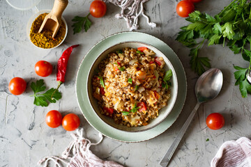 Vegetarian dish: stewed buckwheat with vegetables and fresh herbs in a gray plate on a gray background. Top view