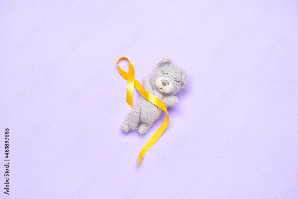 Golden awareness ribbon and toy bear on violet background. International Childhood Cancer Day