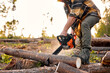 © Roman - Lumberjack logger worker in protective gear cutting firewood timber tree in forest with chainsaw. caucasian male in plaid shirt engaged in hard work in forest at summer evening. Cropped wood man