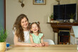 Portrait happy smile family. Mom and daughter at table look at cameras. two sisters laugh At home room and laugh. Place for text. childhood. Caucasian woman and girl in frame. Nanny child Babysitter.