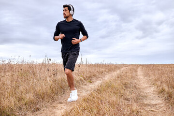 Athletic sportsman enjoy jogging in field, active lifestyle concept. Fit caucasian bearded male in black sportswear is engaged in sport, workout on fresh air, marathon, jogging, running, fitness