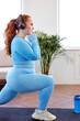 Home activity and training. Overweight woman exercising and listening to music. Fat lady in blue sportive outfit is stretching body, warms up muscles before workout, wearing headphones