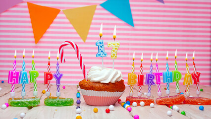 Happy birthday card of 17 years old on a pink background, with a number in a cupcake. Beautiful happy birthday background with number 17 with burning candle. Festive background with colorful decoratio