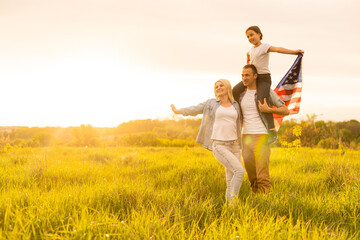 Patriotic holiday. Happy family, parents and daughters children girl with American flag outdoors. USA celebrate 4th of July.