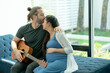 © narong - Man kiss on forehead of pregnant wife also hold guitar in living room after relax activity together and stay at home with love and happiness family.