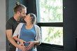 © narong - Pregnant woman and her husband hug and kiss together in front of glass window express love and care for family.