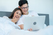 © narong - Asian man and woman look like lover enjoy with laptop and lie on bed and express happy together at home.