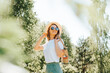 © Sergio - Pretty smiling caucasian young woman with freckles in straw hat, glasses and handbag looking away while standing in nature on sunny summer day. Portrait of happy charming girl walking outdoors