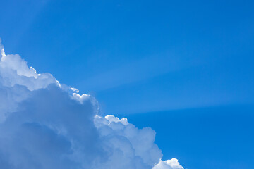 blue sky with a big cloud blocking the sun causing a beam of light to come out of the clouds and coppy space to place the letters for background