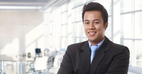 Poster - Confident young asian businessman smiling in modern business office. Portrait of adult man in 30s, happy confident smile. Copy space.