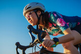 Fototapeta Sport - close up asian woman with athletic body shape in protective helmet and glasses riding bicycle on blue sky