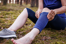 Hiker Putting Elastic Orthopaedic Bandage During Hiking. Woman Feeling Pain Of Joint And Knee After Injury. First Aid Of Torn Ligament Or Knee Sprain Fixation Outdoors