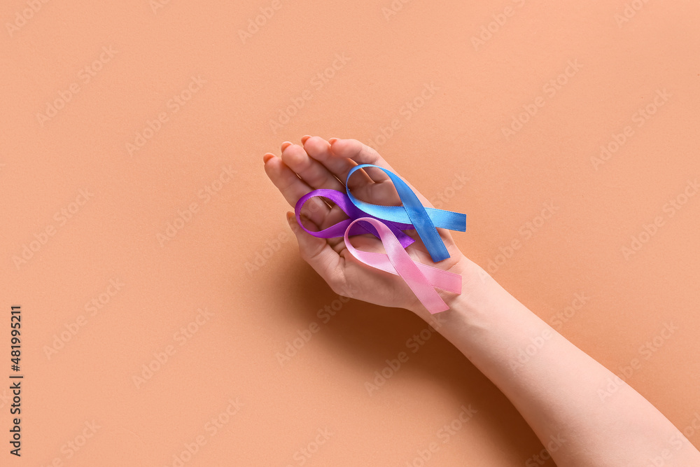 Female hand with different awareness ribbons on beige background. World Cancer Day