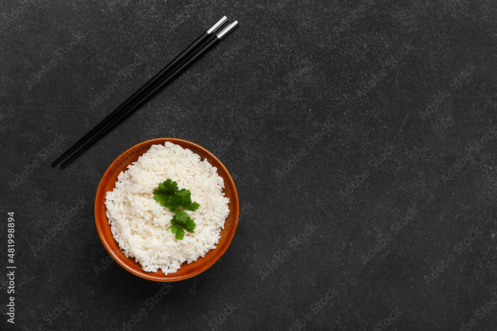Bowl with tasty boiled rice and chopsticks on dark background