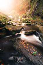 Cascade Waterfall In A Autumn Looking Forest With Leaves On The Ground And Fog In The Air