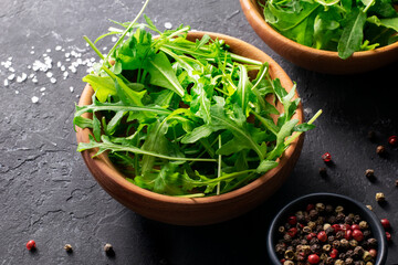 Fresh organic arugula  for salad in wooden bowl on black background close up. Top view.