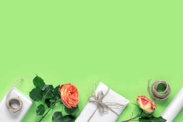 Wall Mural - Gift boxes in wrapping paper, tied with rope, with bouquet of red-yellow roses for congratulations on green background.   Creative holiday present.