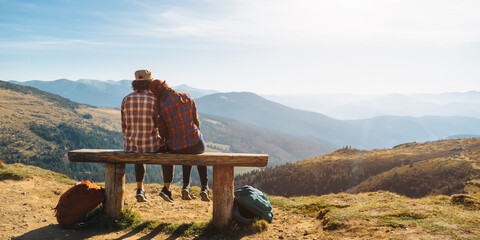 couple of hikers with backpacks enjoying valley landscape view from top of a mountain. young adult t