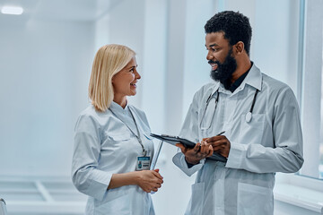 Two doctors dressed in white gowns talking and laughing in the hospital corridor.