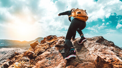 Wall Mural - Successful hiker with backpack climbing the mountain on sunset - Traveler woman standing on the top of the rock pointing the landscape - Freedom, success and extreme sport concept