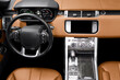 Brown luxury modern car Interior. Steering wheel, shift lever and dashboard. Detail of modern car interior. Automatic gear stick. Part of orange leather seats with stitching in expensive car