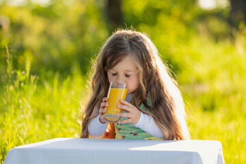 girl drinking juice sitting at the table in nature