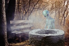 Mysterious Illustration Image Of An Alien Sitting Behind A Fountain With A Wooden Bench In The Misty Forest.
