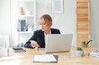 © artmim - Executive wearing suit calling customer service on the phone and sitting on a desk in the office