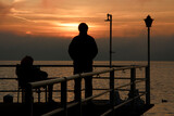 Fototapeta Sypialnia - coppia di persone contemplano il tramonto sul lago