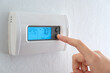 canvas print picture - A woman is pressing the down button of a wall attached house thermostat with digital display showing temperature 70 degree Fahrenheit for heating, cooling, electricity and gas saving