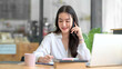 © amnaj - Smiling young Asian businesswoman sitting talking on the phone with laptop computer on desk in the office.