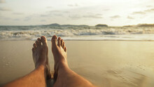 The Man Feet Relaxed Are Lying On The Sandy Beach And Washed By The Water And Foam Of The Ocean