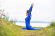 © Pelo Blanco Photo - Athletic woman doing yoga in a grass field overlooking a body of water.