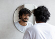 © Prostock-studio - Handsome indian guy looking at his reflection in the mirror, standing in modern bathroom at home