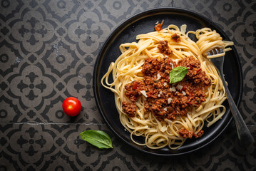 Wall Mural - Pasta spaghetti bolognese with minced beef sauce, tomatoes, parmesan cheese and fresh basil in a plate on black tile background. Italian food, top view