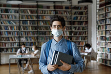Freshman Student In Medical Protective Mask, Glasses And Backpack Visiting Library, Holding Stack Of Books, Textbook, Looking At Camera, Protecting Lower Face, Staying Safe From Infection