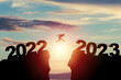 © Dilok - Welcome merry Christmas and happy new year in 2023,Silhouette Man jumping from 2022 cliff to 2023 cliff with cloud sky and sunlight.