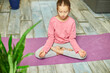 © bondarillia - Cute little girl sitting on fitness mat in a lotus position while doing yoga at hom