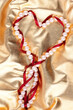 White beads and a red heart-shaped silk ribbon on a golden background