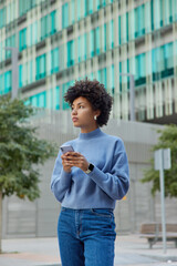 Wall Mural - outdoor shot of thoughtful beautiful woman wears casual blue jumper and jeans stands against urban s