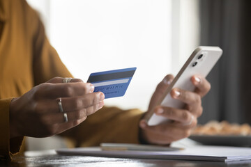 Woman holding smartphone, using credit card, shopping online with ecommerce app, making payment, buying on internet store websites, paying for virtual purchase, spending money. Close up of hands