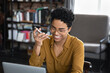 © fizkes - Happy Afro American entrepreneur woman recording audio message on mobile phone at home workplace. Business woman, self employed worker having telephone call on speaker, using voice recognition app