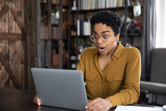 Shocked excited young African business professional woman getting unexpected news, staring at laptop display with open mouth, having problems with software, feeling stress about app or services errors