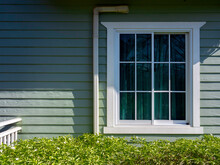A White House Window With Glass, Green Curtain Decoration On The Small Light Green Wooden Resident With Copy Space, View From Outdoor.