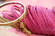 close up of gold bangle and dozens of pink glass decorative bangles spread on pink saree