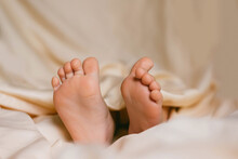 Children's Feet On A White Bed. Infant Baby Is Sleeping In His Crib. Importance Of Sleep For Babies. Sleep Mode Babies 3 Y.o.