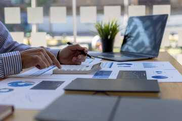 Wall Mural - Businessman using a calculator to calculate numbers on a company's financial documents, he is analyzing historical financial data to plan how to grow the company. Financial concept.