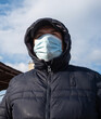 © bogdan vacarciuc - Man dressed in winter jacket and hood on his head, wearing a protective mask on the street. Wearing a protective mask while coronavirus outbreak.