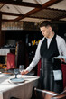 © Andrii - A young male waiter in a stylish uniform is engaged in serving the table in a beautiful gourmet restaurant. A high-level restaurant. Table service in the restaurant.