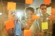 © opolja - Diverse group of businesspeople standing in an office brainstorming together with sticky notes on a glass wall